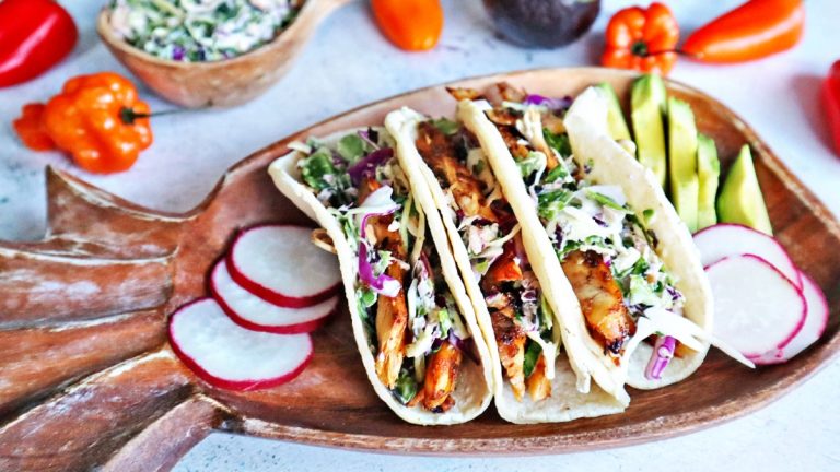 Jerk chicken tacos on a wooden plate with radishes.