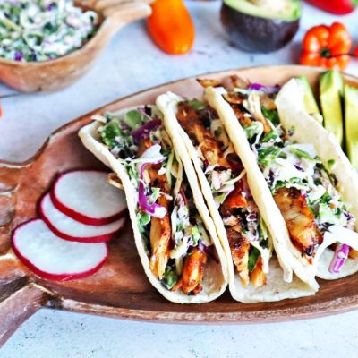Jerk chicken tacos on a wooden plate with radishes.