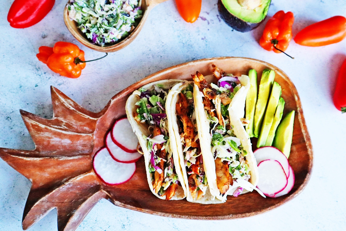 Jerk chicken tacos on a wooden plate with radishes.