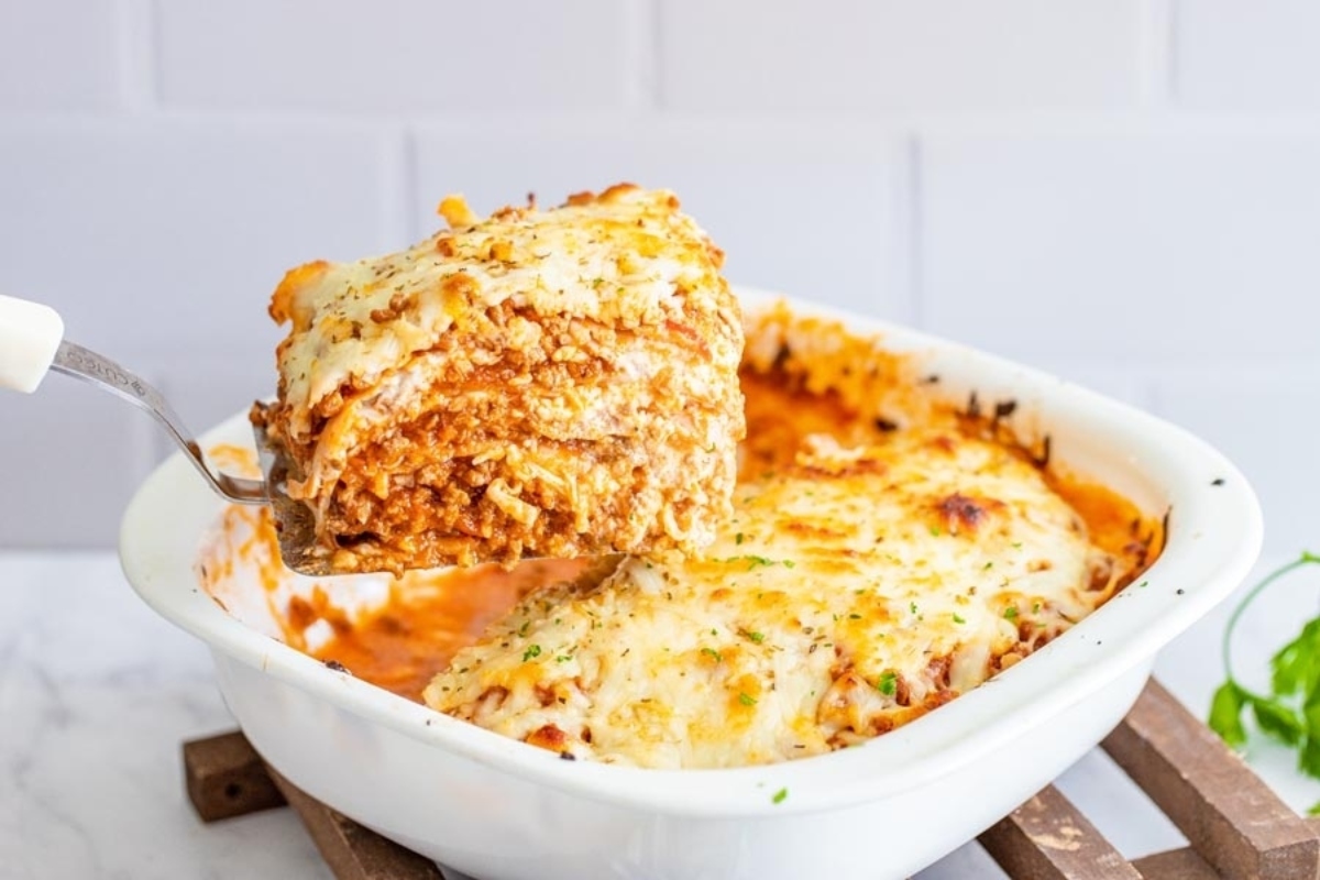 Low carb lasagna being taken out of a white baking dish.