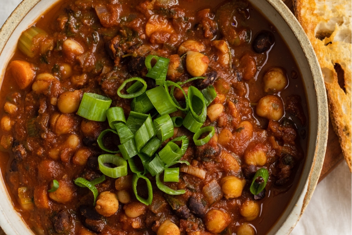 A bowl of bean and chickpea stew with bread, perfect for chili lovers.