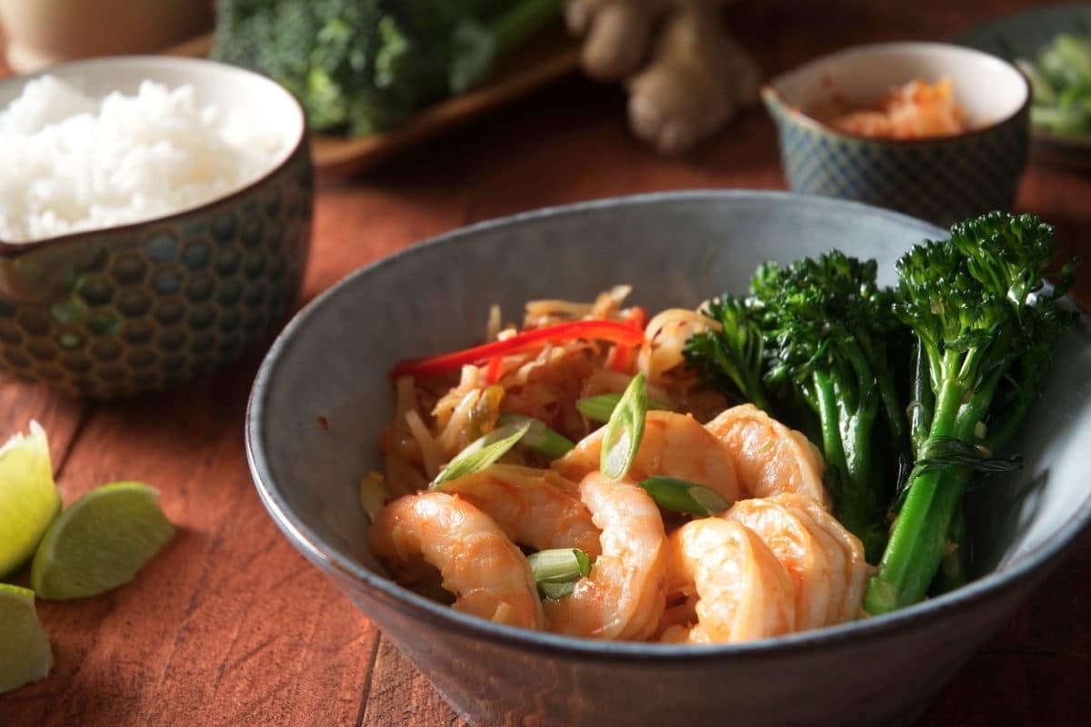 A bowl of shrimp, broccoli and rice on a wooden table, perfect for dinners.