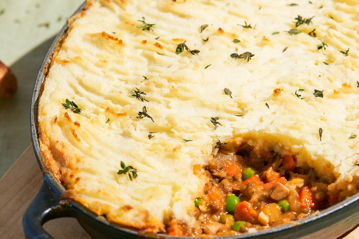 A loaded dish of shepherd's pie featuring vegetables on a wooden cutting board.
