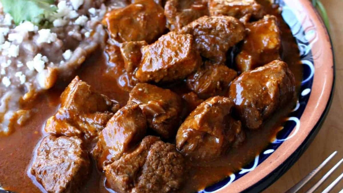 A bowl of beef stew with rice and beans on a wooden table.