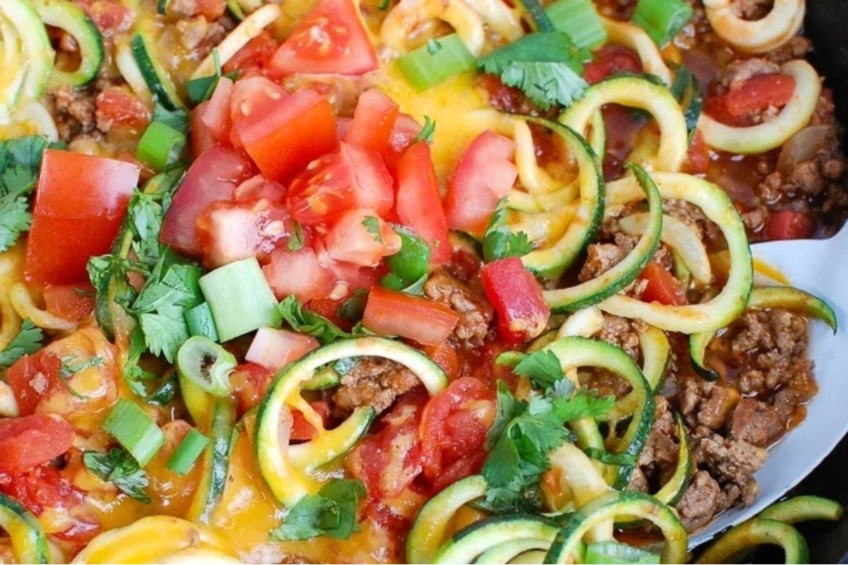 A spiralizer recipe featuring a skillet filled with zucchini and meat.