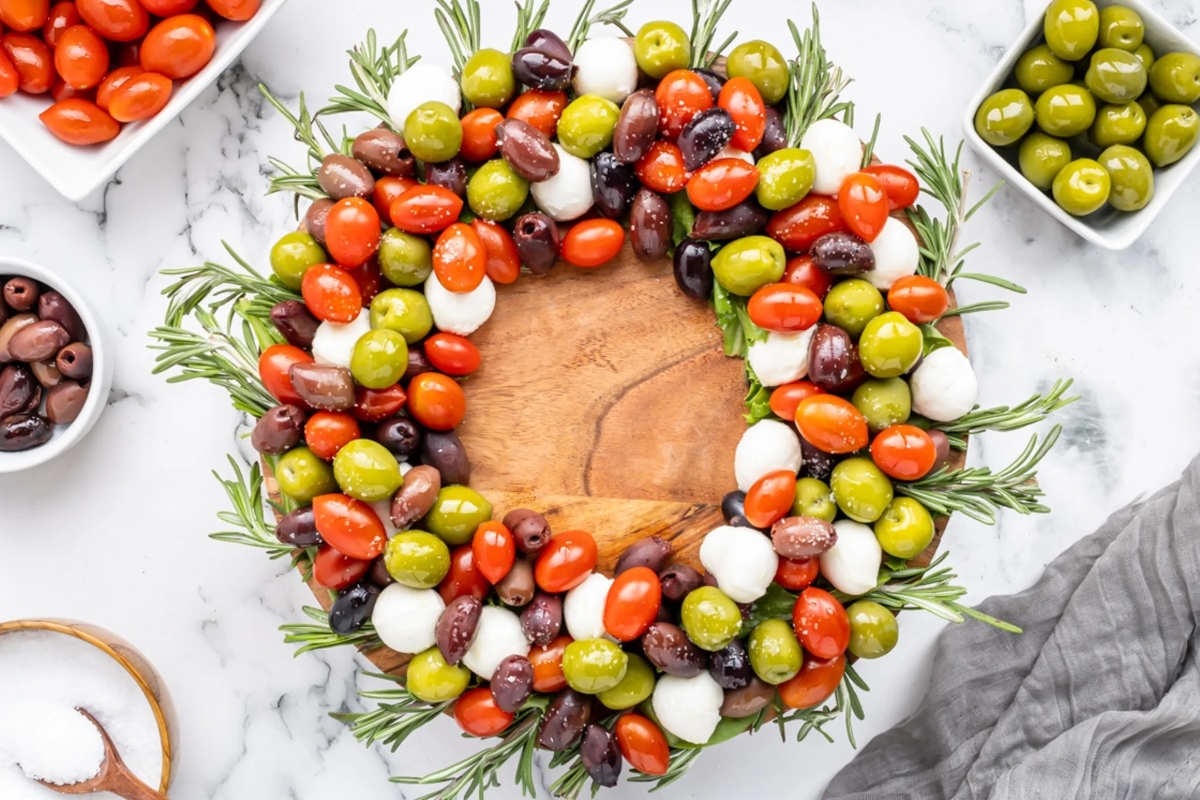 A festive wreath of olives and tomatoes on a wooden board, perfect for Christmas appetizers.
