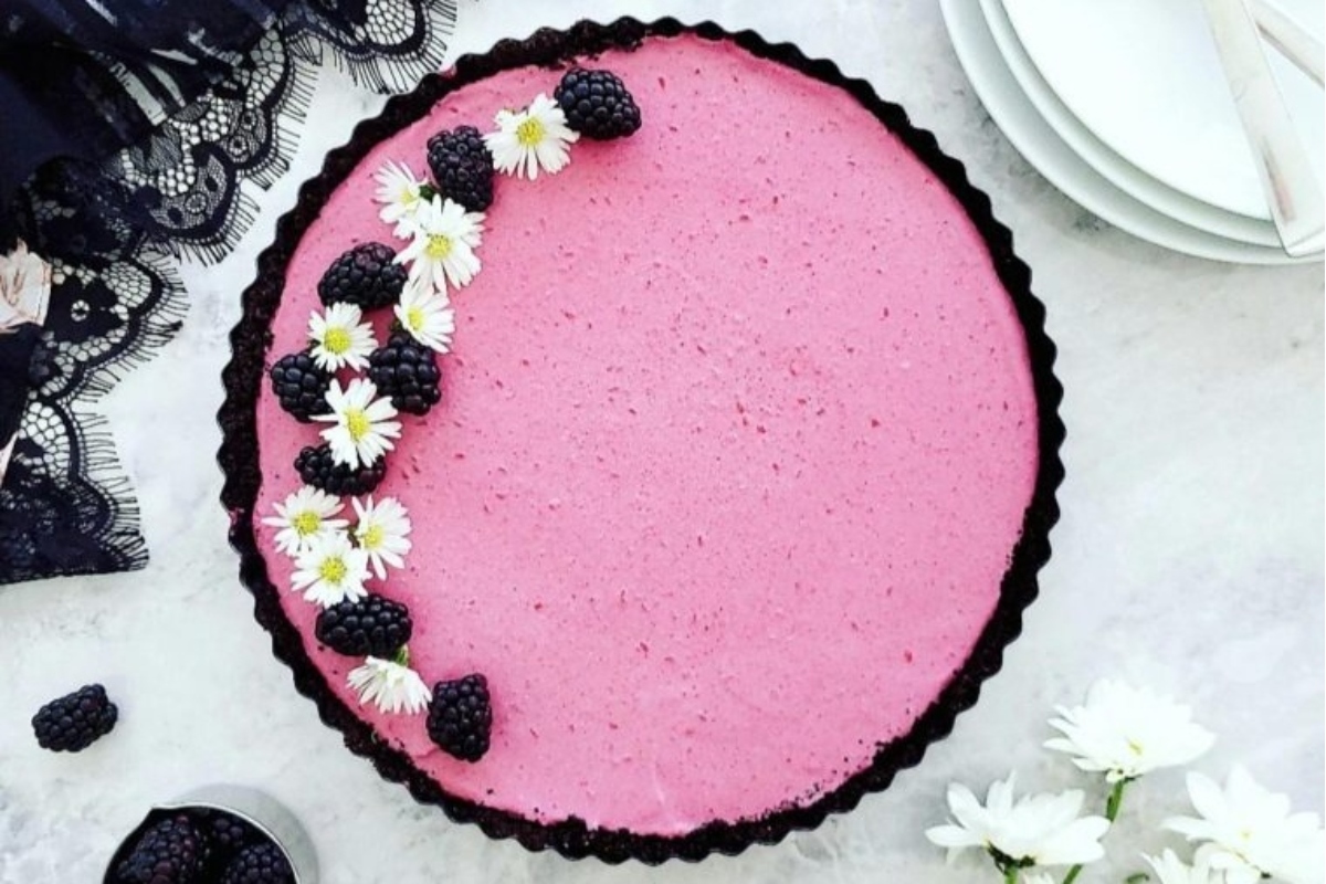 A scrumptious pink tart adorned with vibrant daisies and juicy blackberries.
