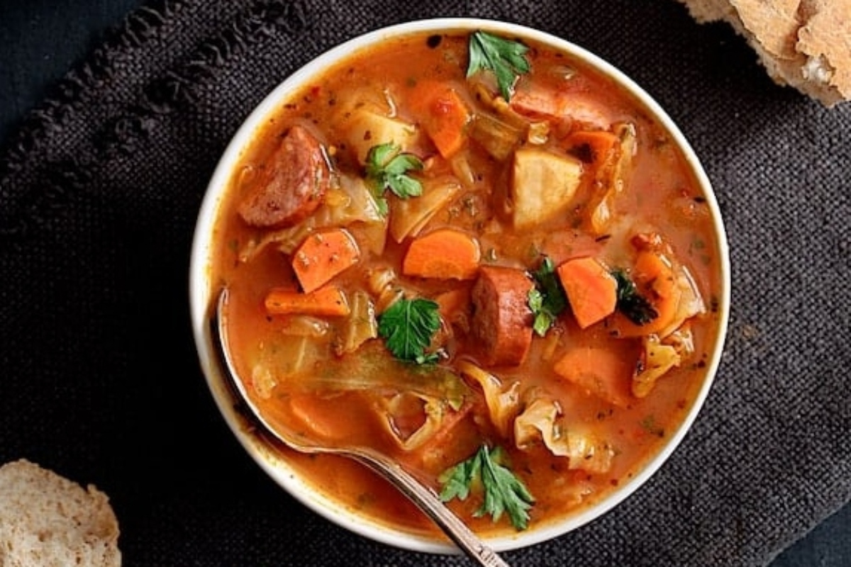 A hearty bowl of potato soup with sausage, carrots and bread.