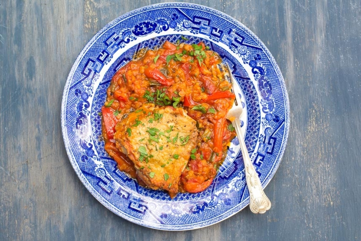 Chicken thighs cooked in a tomato sauce served on a blue and white plate.