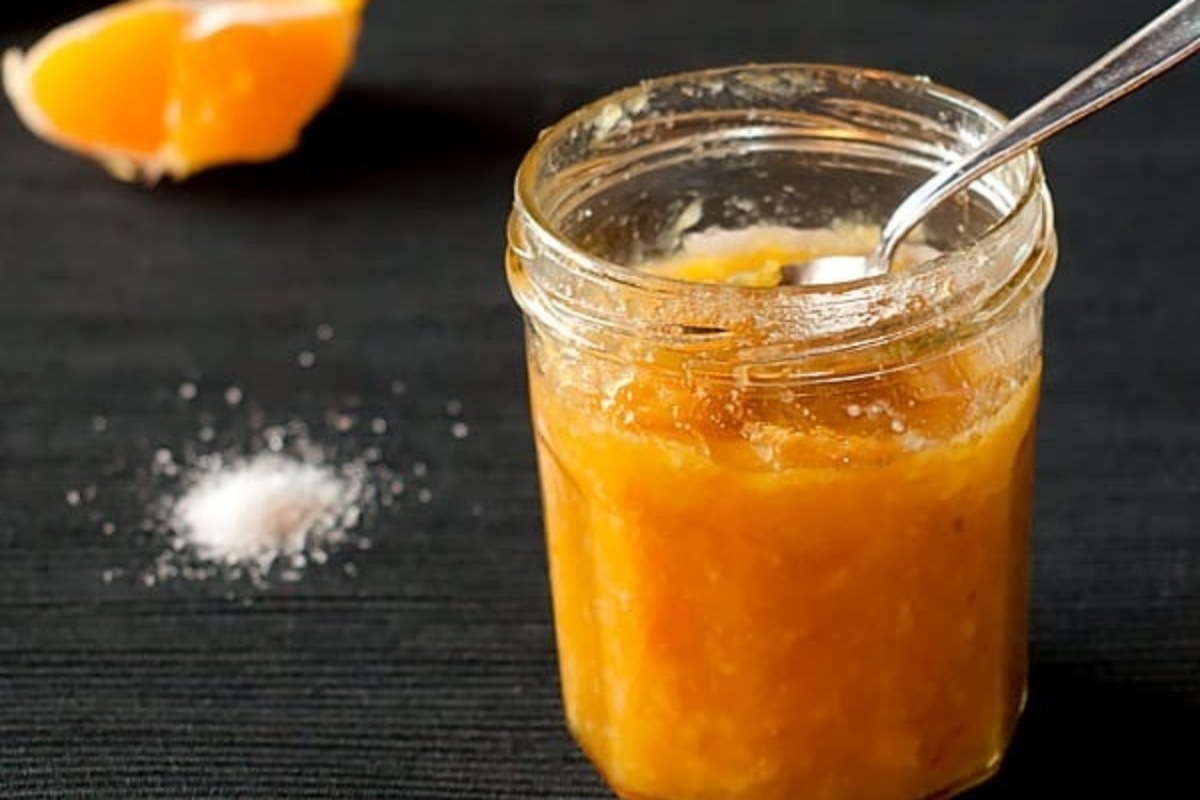 A jar of orange sauce, perfect as a gift for food lovers, with a spoon next to it.