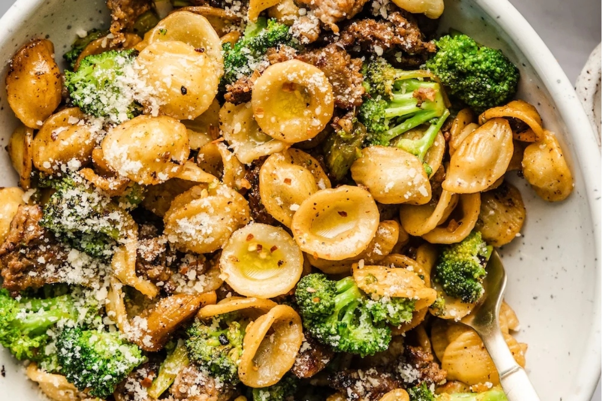 A savory recipe featuring a bowl of pasta with deliciously cooked broccoli, meat, and a generous sprinkle of Parmesan cheese.