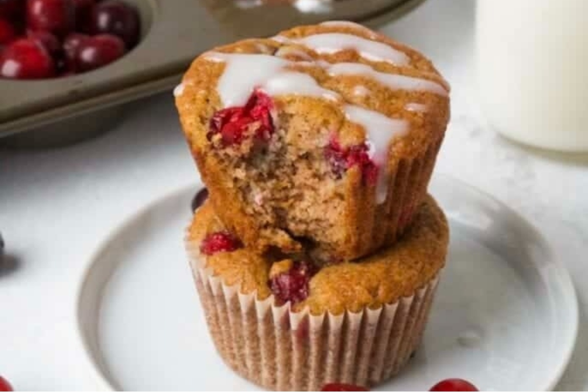 A stack of cranberry muffins on a plate with cranberries. These delicious snacks are made with a special cranberry recipe that will satisfy your cravings.