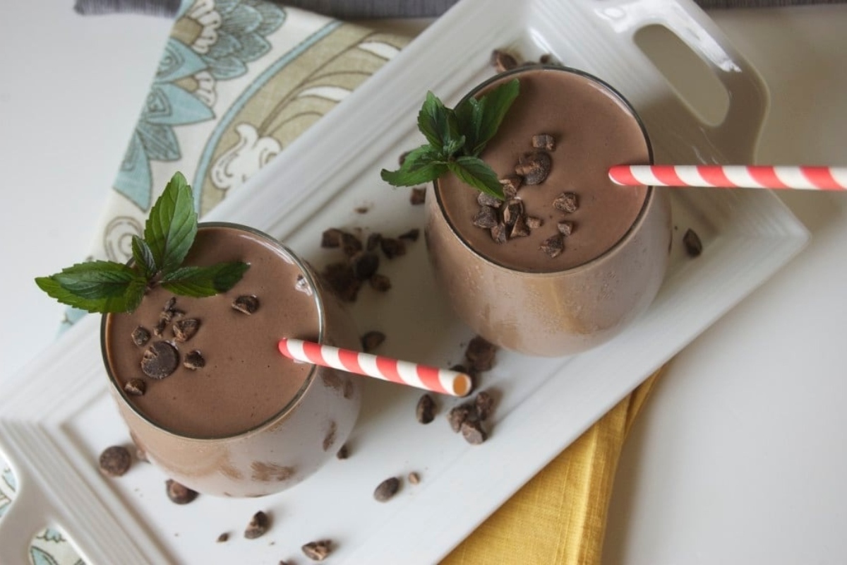 Two chocolate smoothies on a white plate with peppermint leaves.