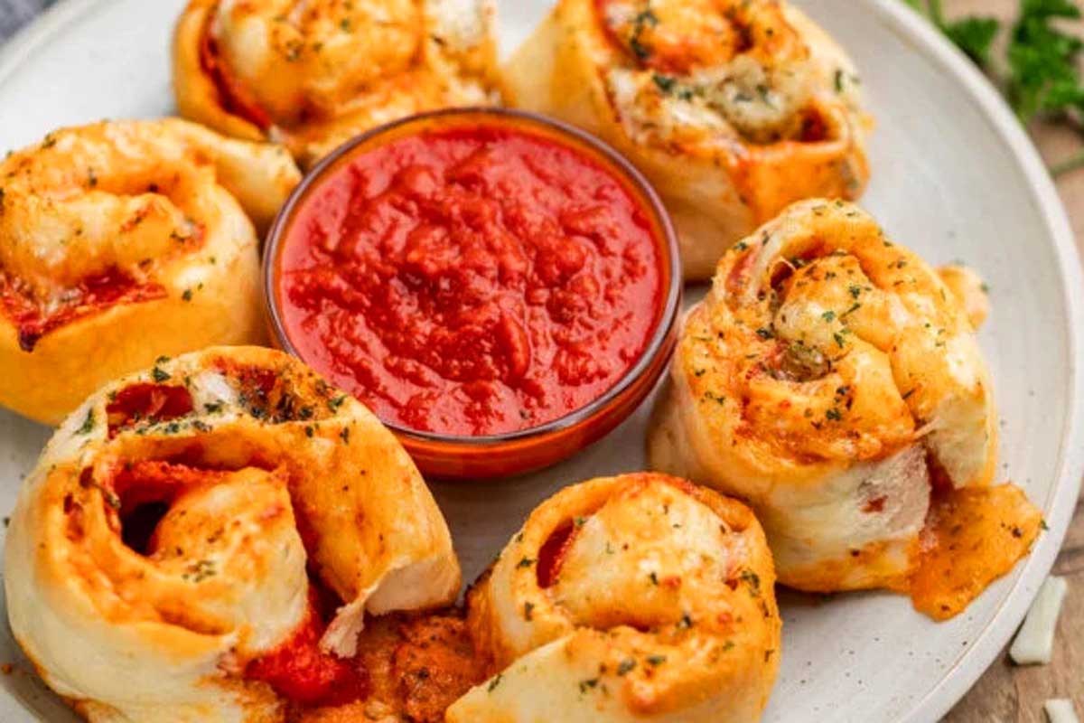 A plate of Italian appetizer pizza rolls with a side of sauce and dipping sauce.