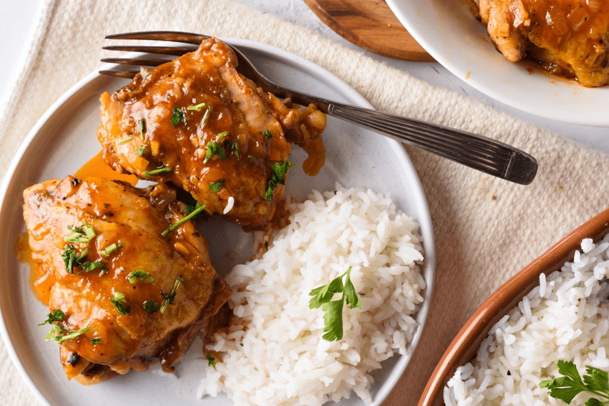 A skillet of chicken with rice and sauce on it, made with succulent chicken thighs.