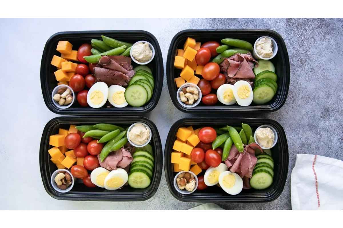 Four healthy black plastic containers with high protein lunches consisting of meat, eggs, and vegetables.