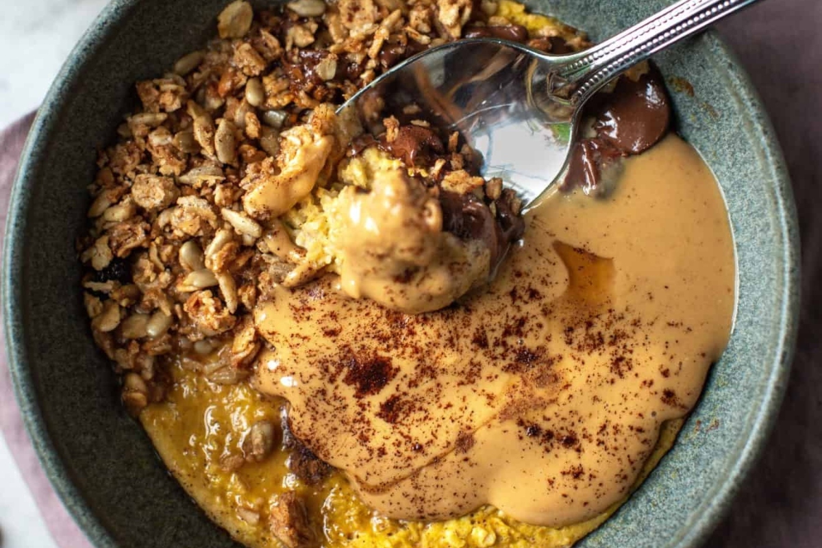 A Healthy bowl of oatmeal with granola and a spoon.