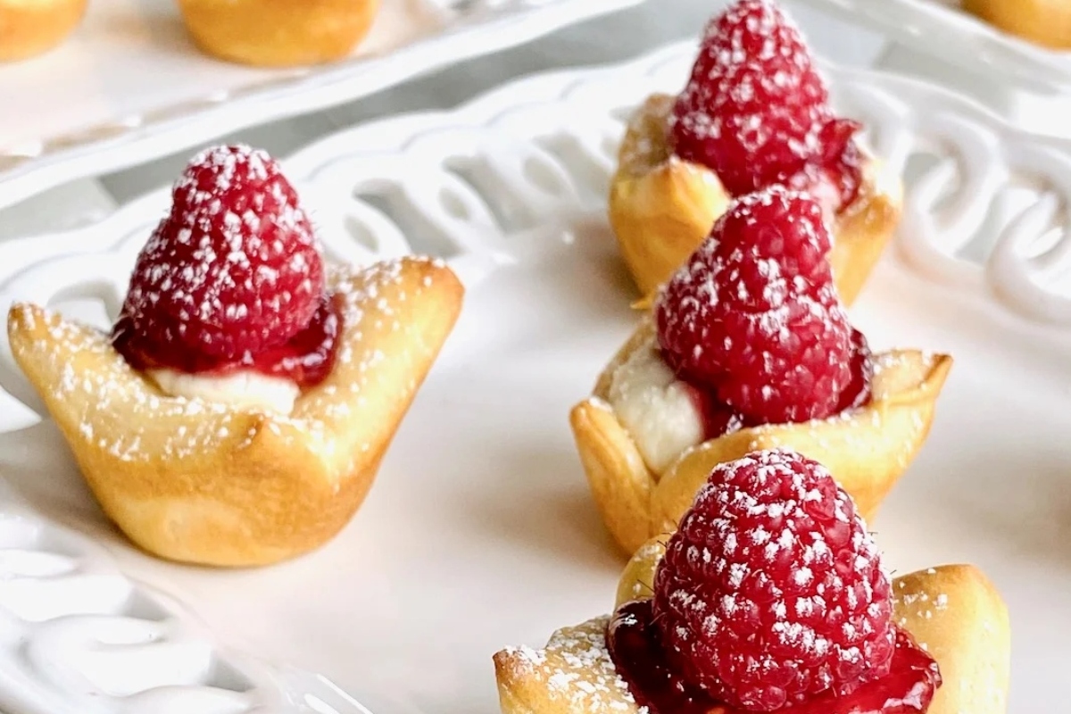 Goat cheese mini pastries topped with raspberries and cream on a white plate.