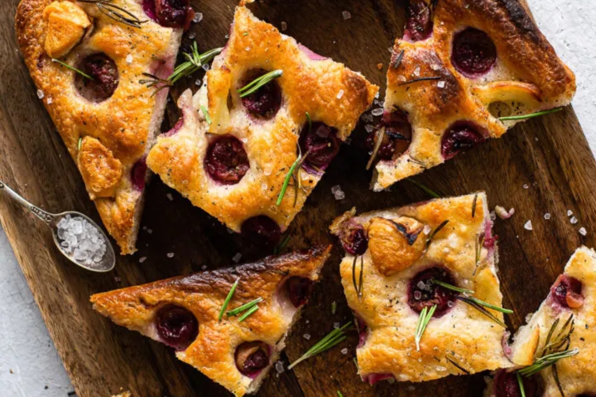A slice of cherry tart with rosemary on a wooden cutting board.