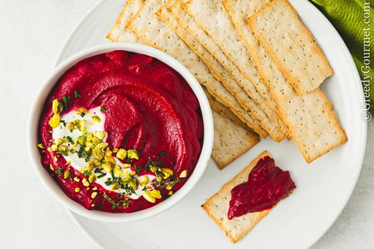 Beet hummus with crackers on a white plate, perfect for beet recipes.