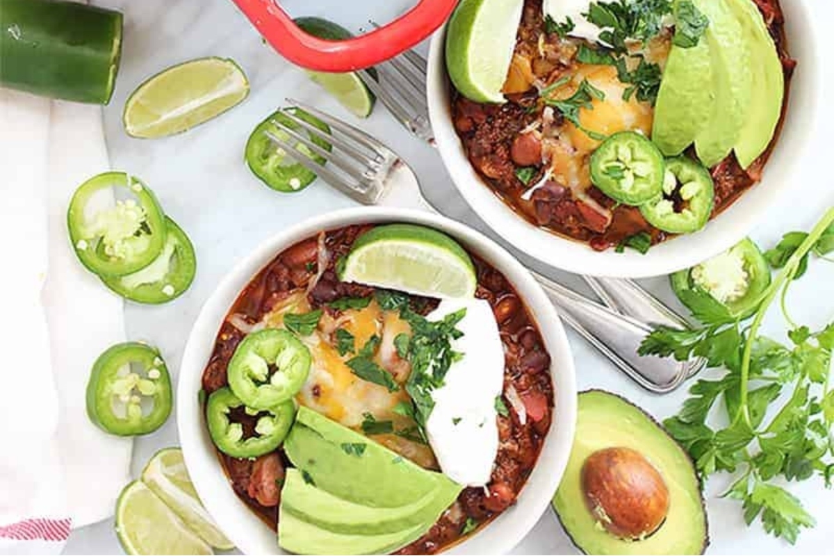 Two bowls of chili with avocados and limes, showcasing delicious Chili Recipes.