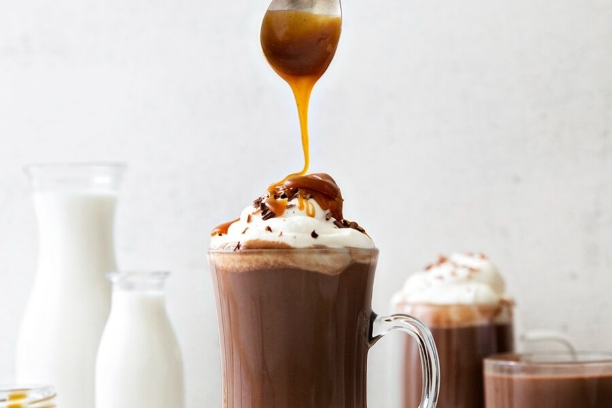 A steaming cup of cocoa with caramel drizzled over it.