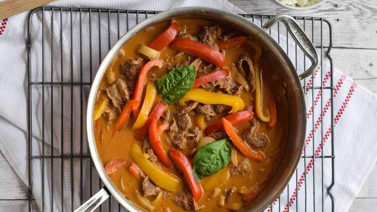 A comforting Thai beef curry recipe cooked in a pan with peppers and basil.