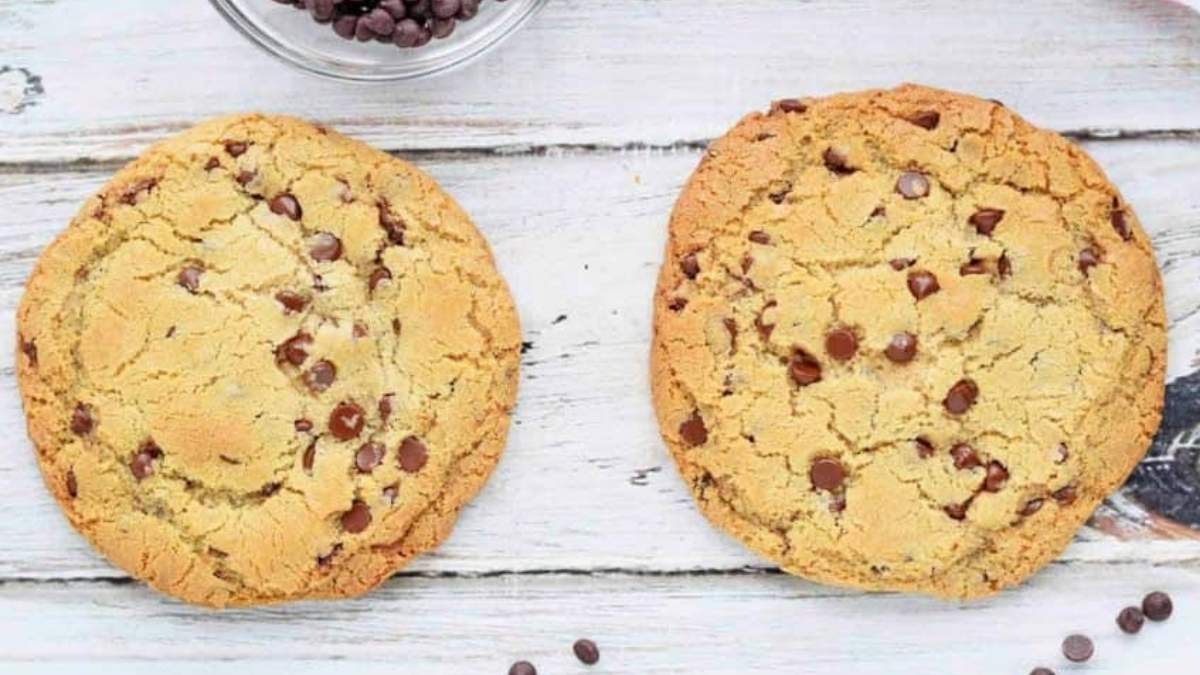 Two chocolate chip cookies, made from a delicious cookie recipe, are placed on a rustic wooden table.