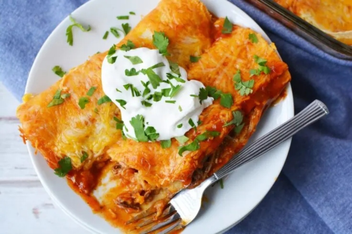 Warm Mexican enchiladas on a plate with sour cream.