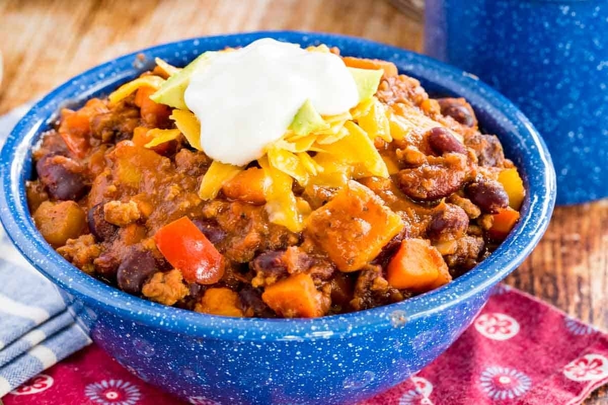 Slow cooker chili recipe served in a blue bowl with sour cream and avocado.