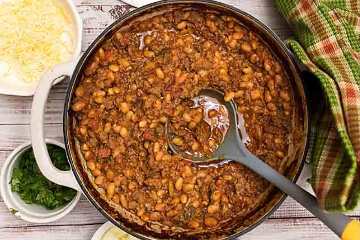 A mouthwatering pot of Chili Recipes with cheese and other ingredients on a wooden table.
