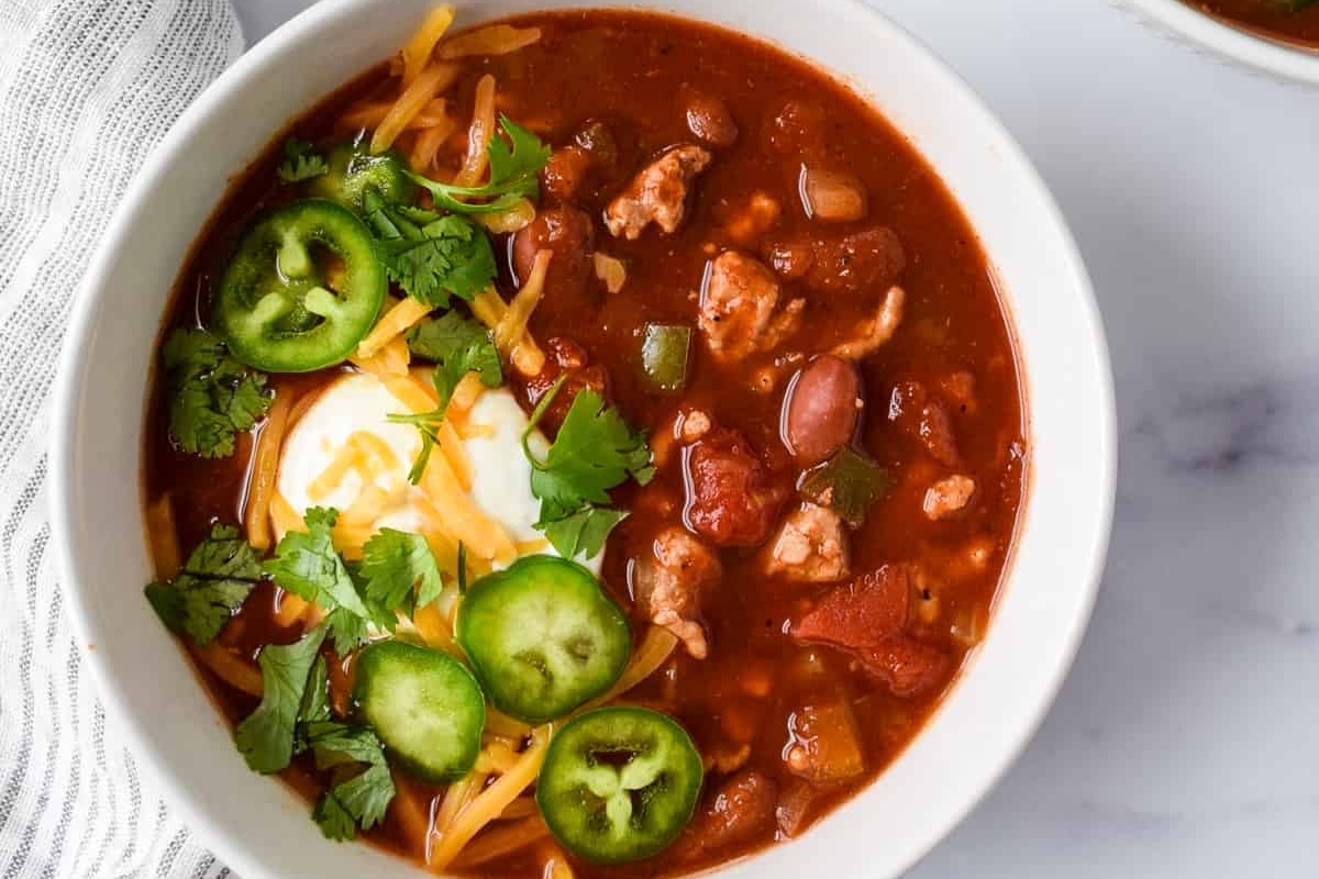 Looking for delicious chili recipes? Look no further! Enjoy a steaming hot bowl of chili garnished with creamy sour cream and fiery jalapenos.