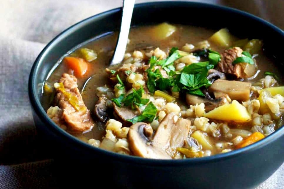 A bowl of chicken barley soup with mushrooms and parsley.