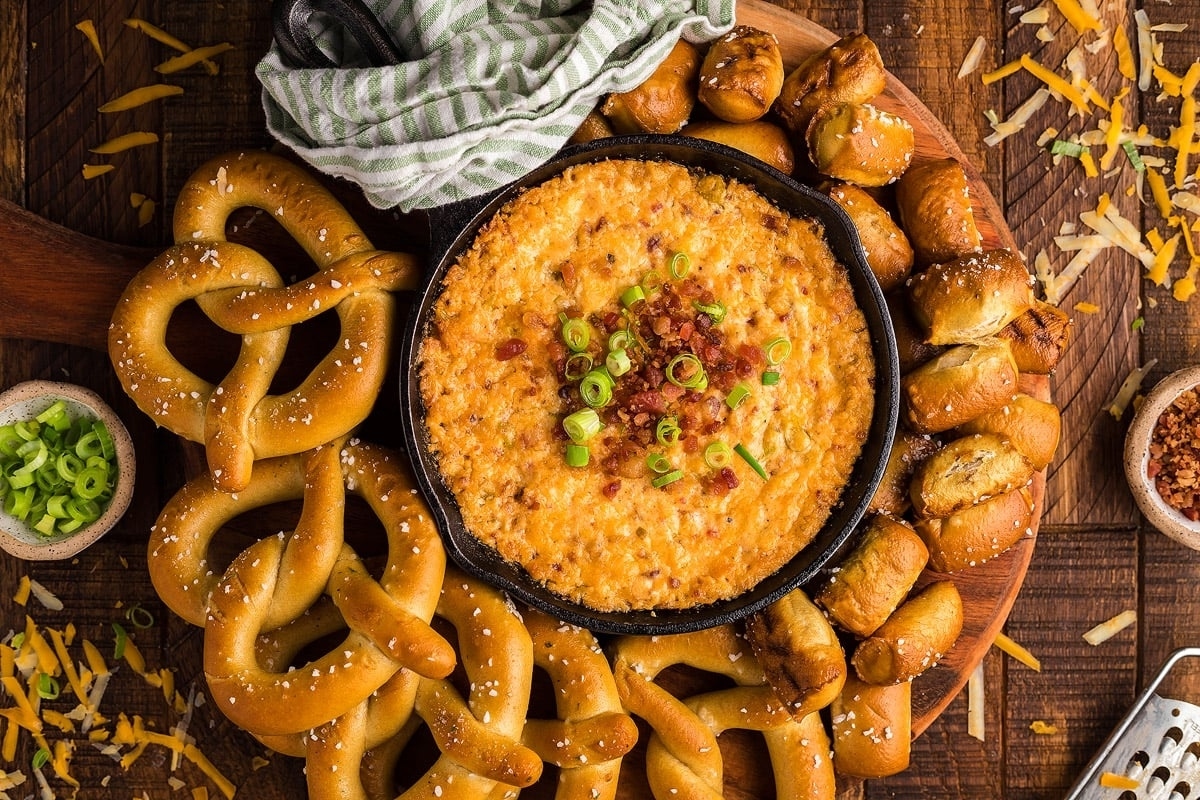 An appetizing bowl of dip with pretzels and pretzel sticks on a wooden table.
