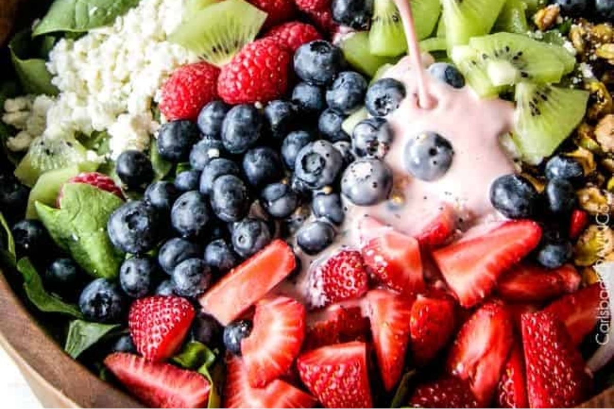 A spinach salad with berries, kiwi, and granola in a wooden bowl.
