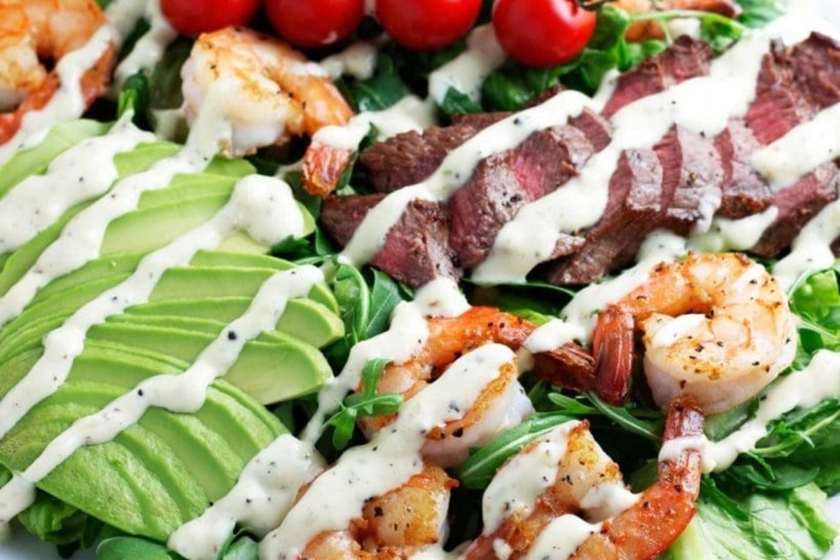 A surf and turf salad with shrimp, avocado, tomatoes and dressing.