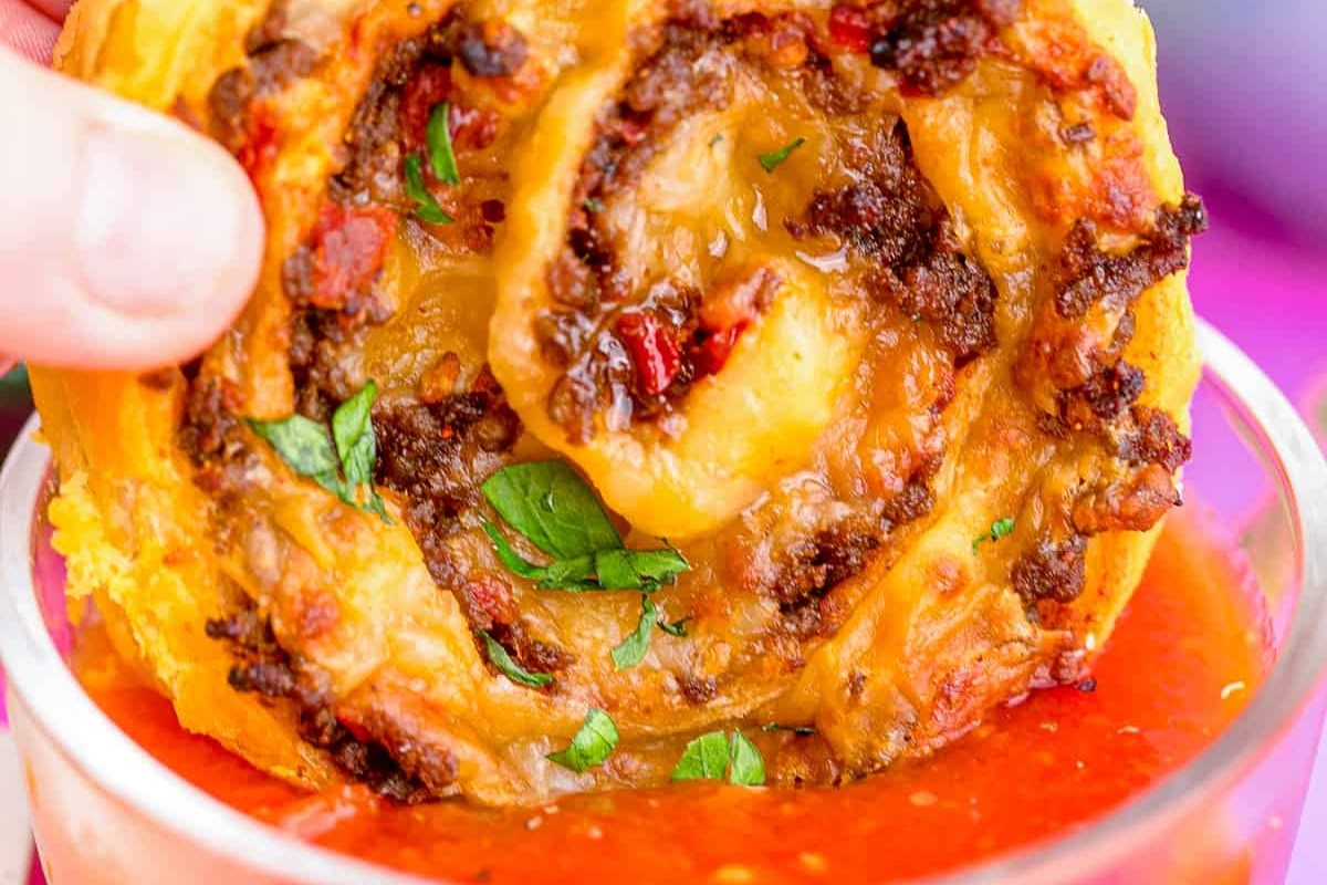 Bite-sized pizza rolls immersed in a glass of tomato sauce.