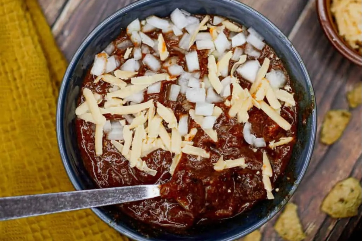 A flavorful chili recipe served with onions and complemented by a spoon.