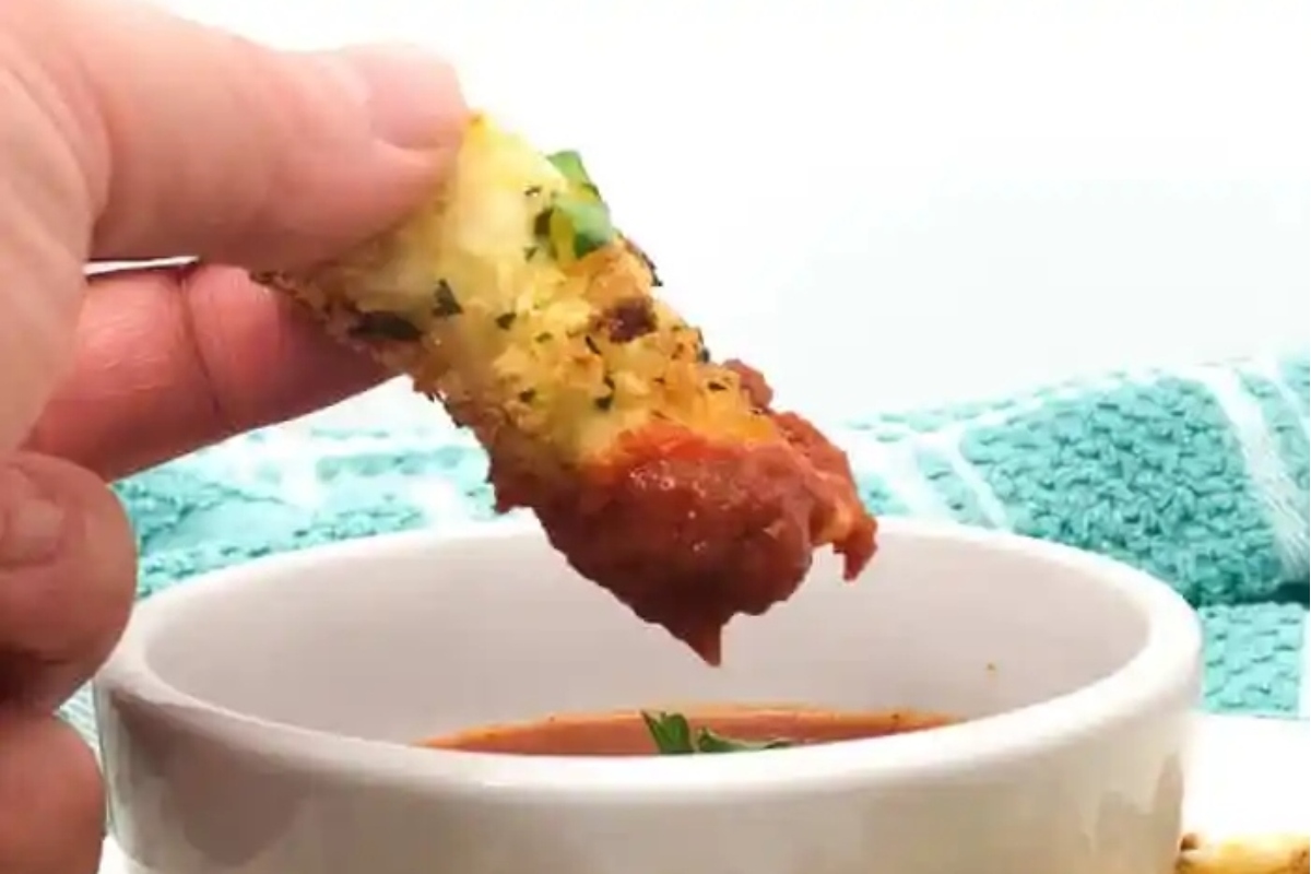 A person enjoying bite-sized breadsticks dipped into a bowl of tomato sauce during game day.