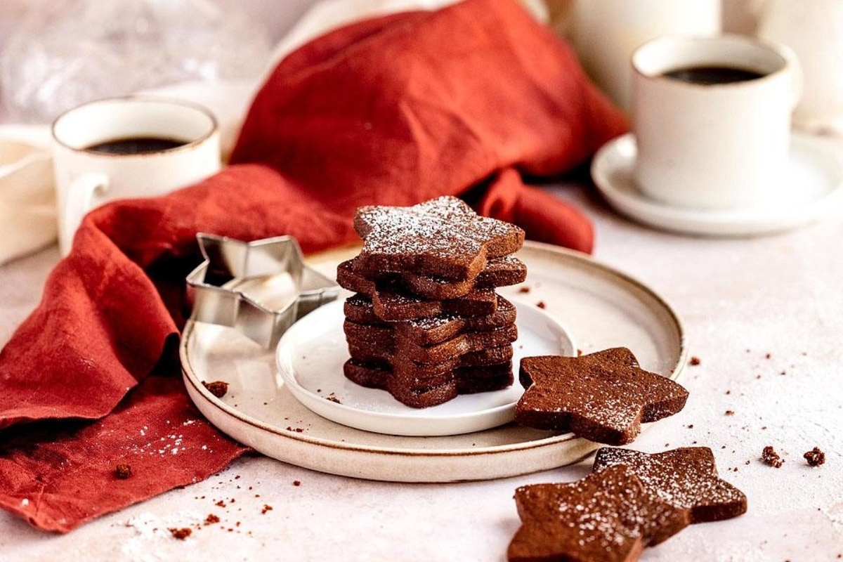 A plate of Christmas sugar cookies decorated with cut out shapes, accompanied by a cup of coffee.