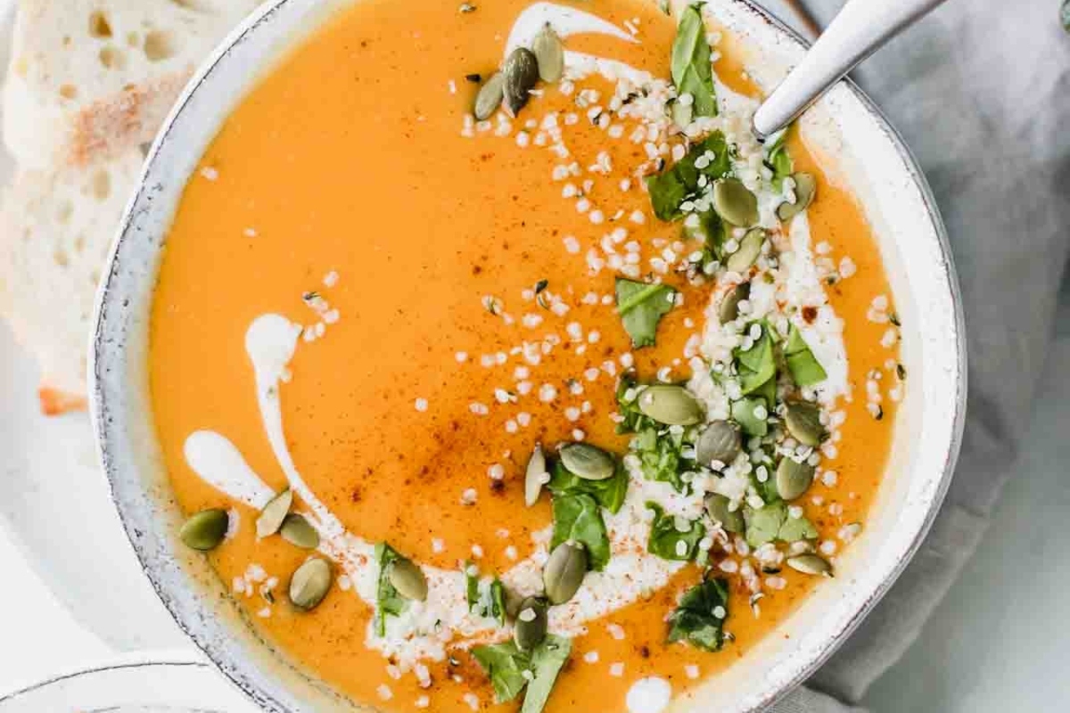 A bowl of delicious pumpkin soup garnished with sour cream and a sprinkling of fresh herbs. This recipe is the perfect way to warm up on a chilly day.