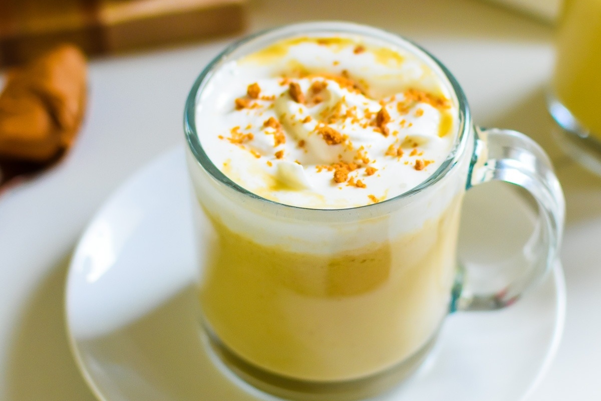A latte with cinnamon and whipped cream topped with cocoa on a white plate.