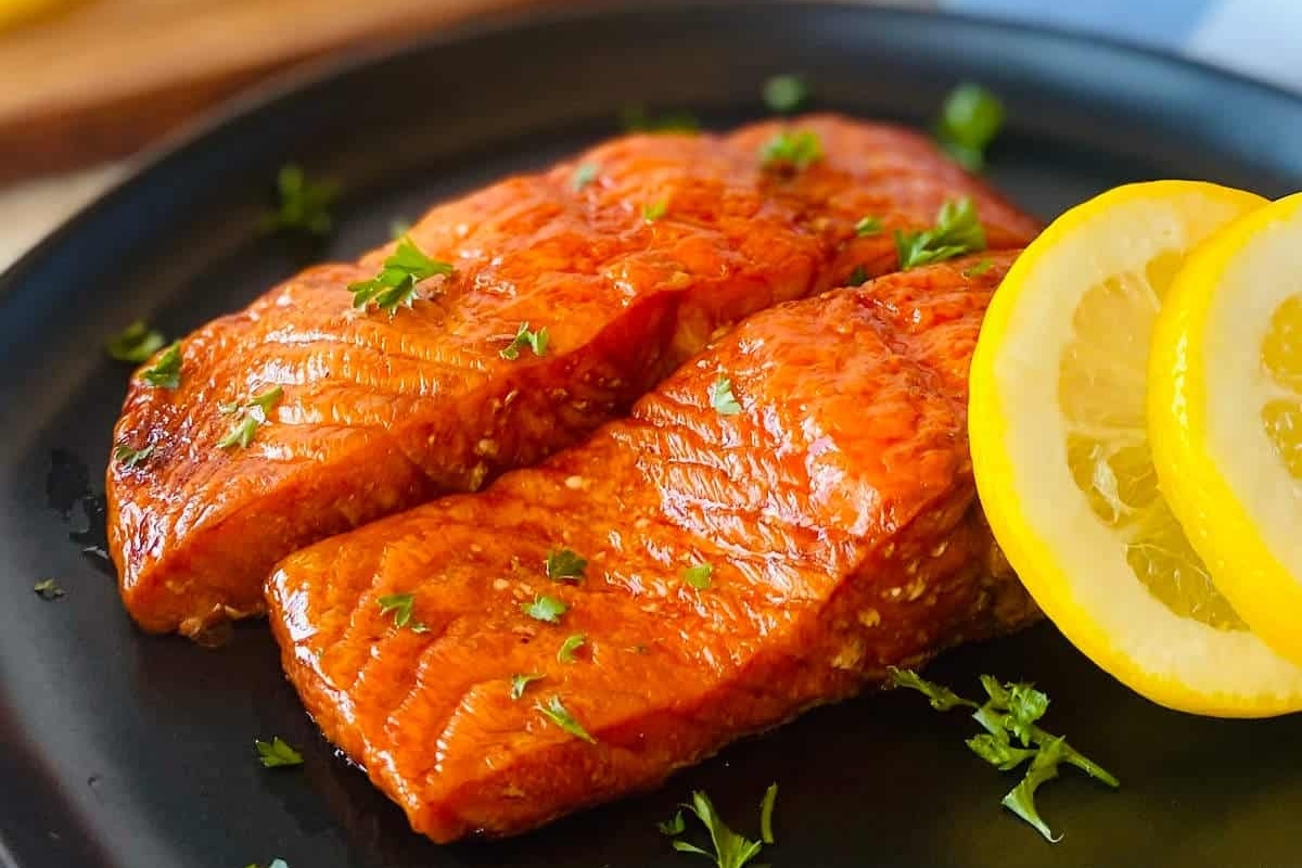 Two salmon fillets garnished with lemon slices on a black plate.