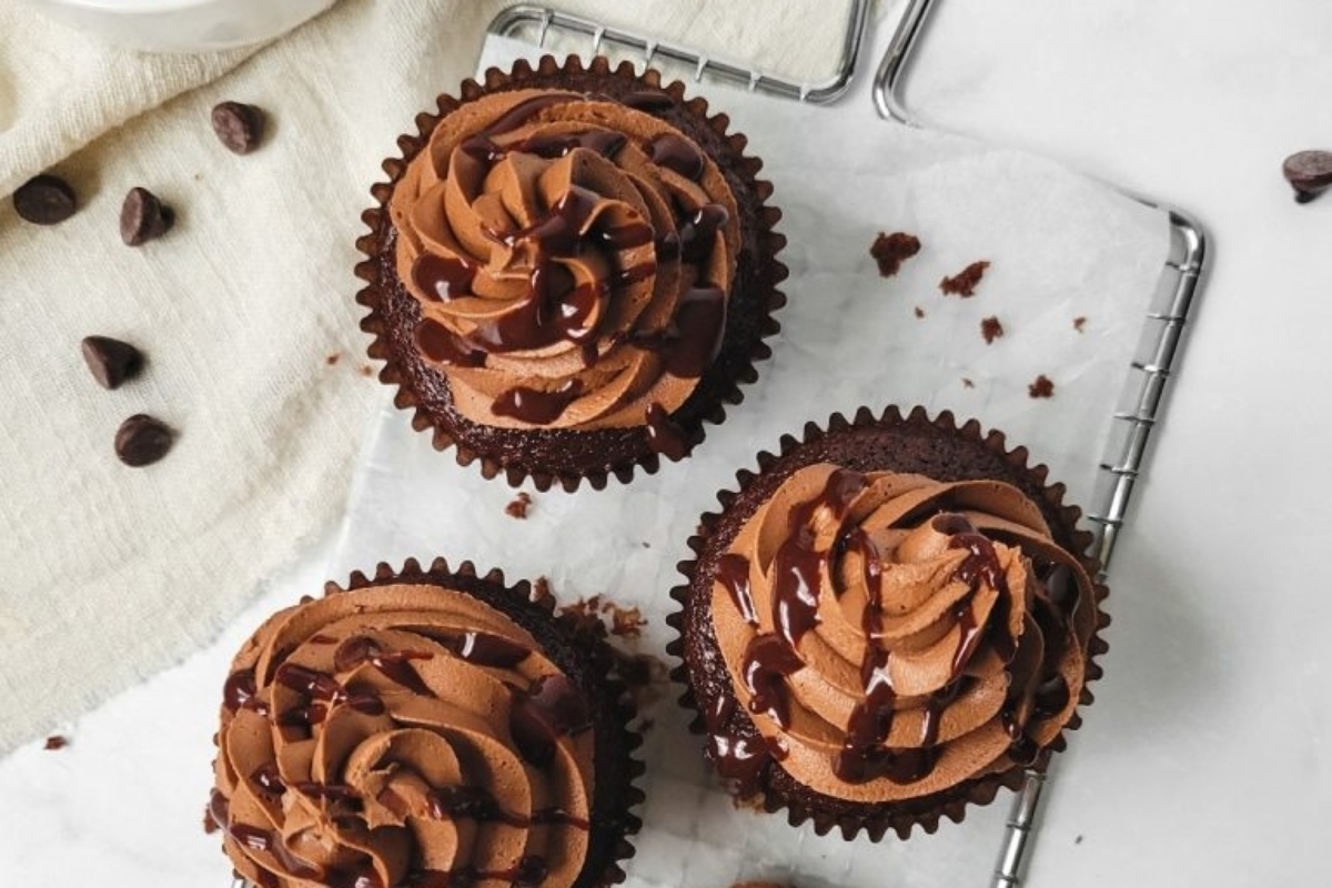 Three chocolate cupcakes with chocolate frosting on a tray.