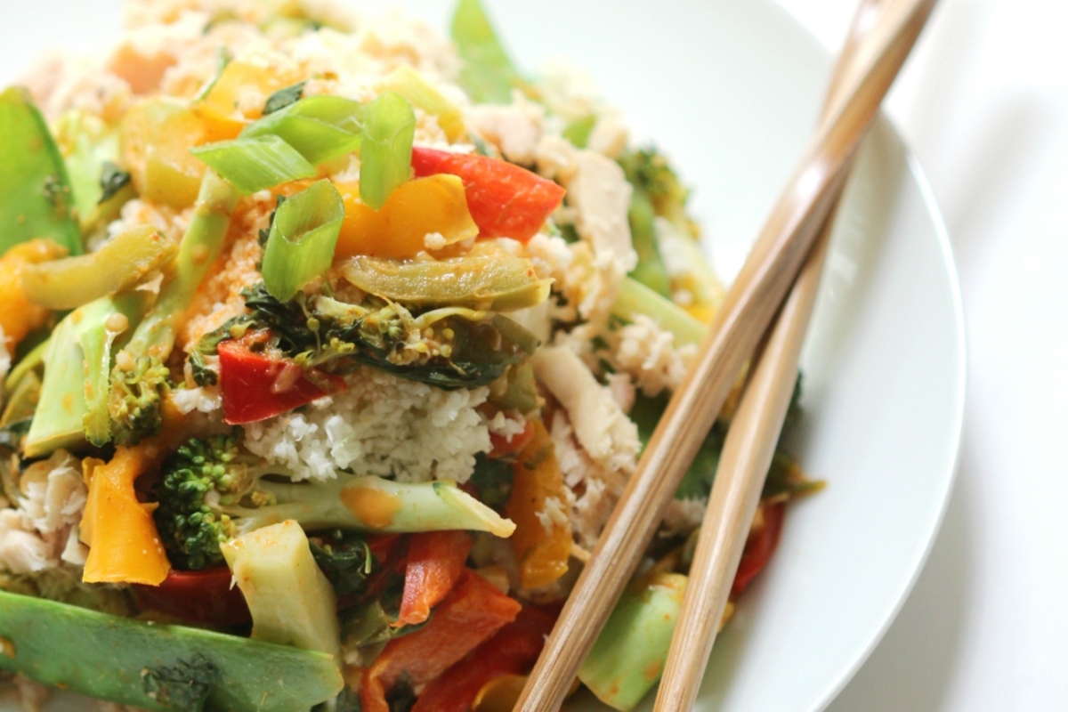 A white plate with rice, vegetables and chopsticks topped with a delicious fish recipe.