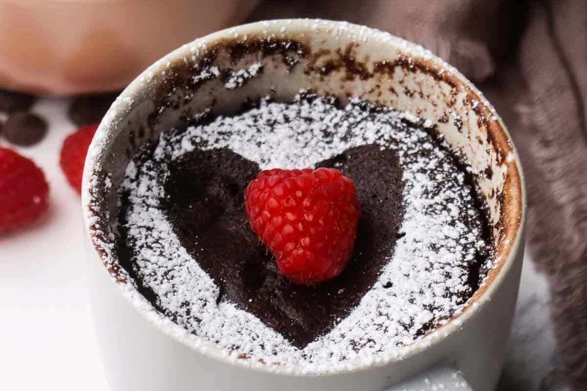 A mug of chocolate pudding drizzled with raspberries and dusted with powdered sugar.