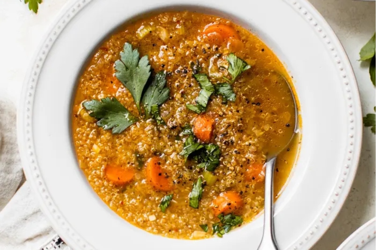 A bowl of vegetable soup with quinoa, carrots, and parsley.