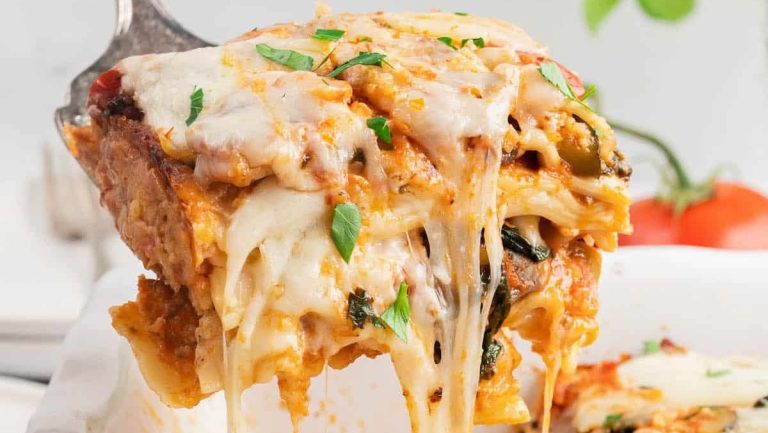 A vegetable-loaded lasagna being gracefully lifted out of a casserole dish.