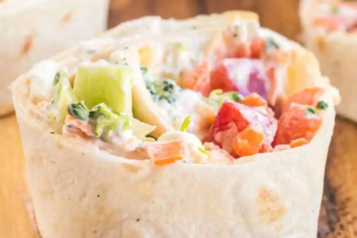 Bite-sized chicken burrito wraps on a wooden cutting board.