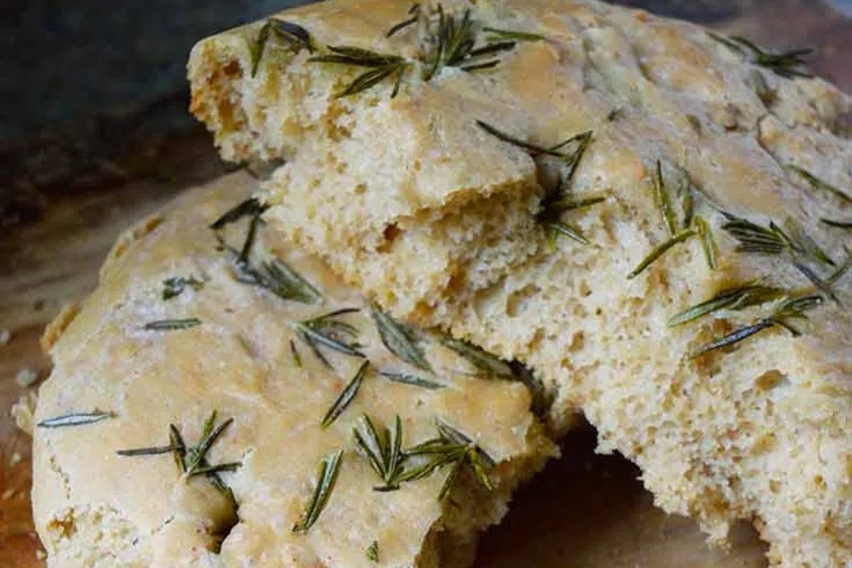 Rosemary sourdough bread with rosemary sprigs on a cutting board near focaccia recipes.